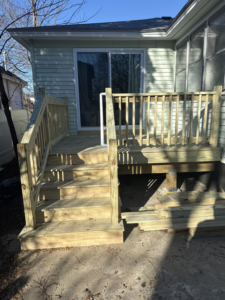 A newly constructed wooden deck with stairs and railings leading to a house, built by Men Construction in Lowell, MA.