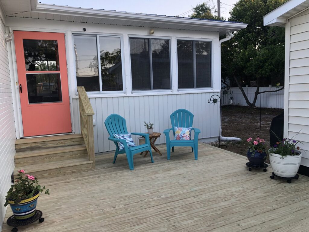 A newly built wooden deck with a sunroom addition, featuring blue Adirondack chairs by Seaside Craftworks LLC in Wilmington, NC.