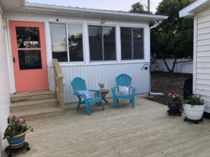 A newly built wooden deck with a sunroom addition, featuring blue Adirondack chairs by Seaside Craftworks LLC in Wilmington, NC.