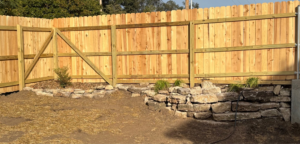 Newly installed wooden fence with a gate and decorative rock wall landscaping by MHK Yard & Gravel in Manhattan, KS