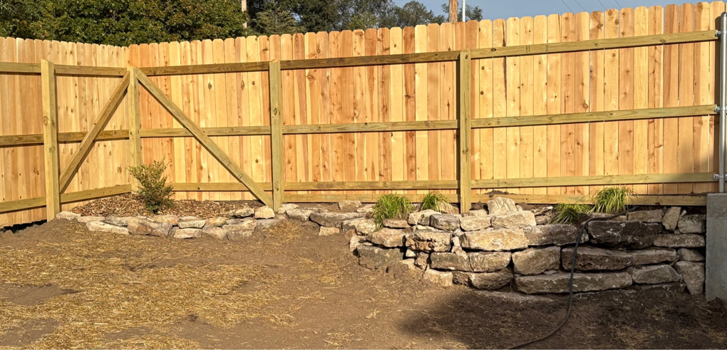 Newly installed wooden fence with a gate and decorative rock wall landscaping by MHK Yard & Gravel in Manhattan, KS