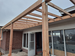 A newly constructed wooden patio cover frame attached to a brick house by Honey Don'ts Handyman Service in Twin Falls, ID.
