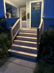A newly constructed wooden porch with stairs and railings leading to a blue front door by Blackcap Handyman in Portland, ME.