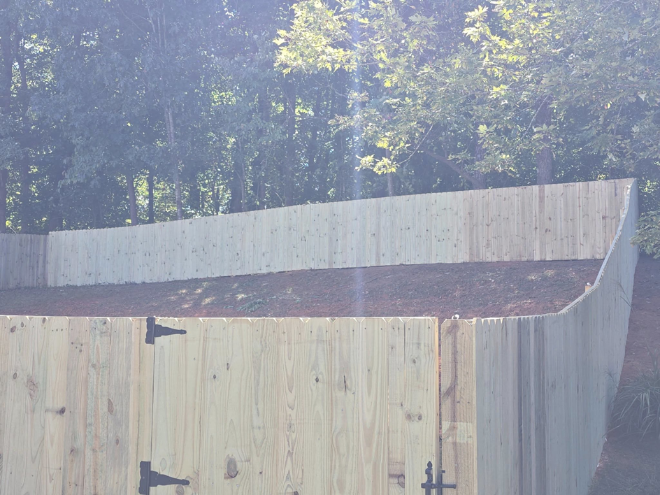 A newly installed wooden privacy fence and gate on a sloped backyard by S&L Decking and Fencing in Charlotte, NC.