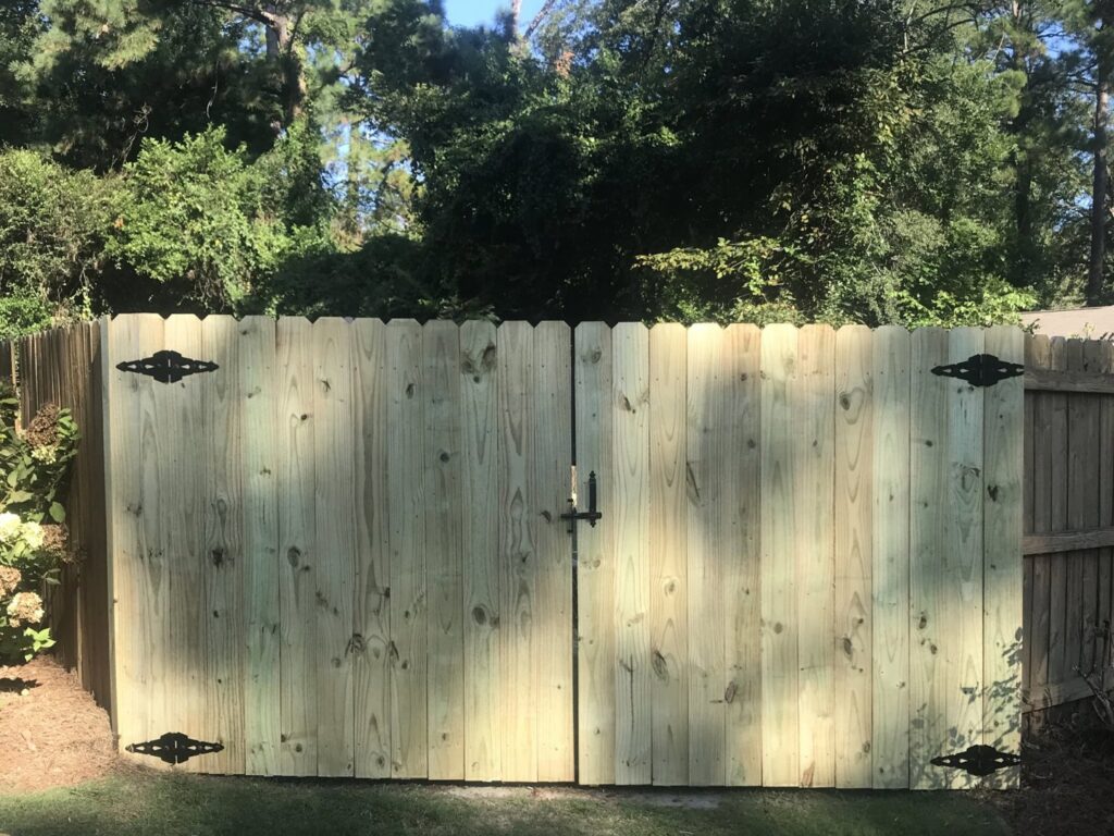Newly installed wooden privacy fence gates with decorative black hardware, demonstrating gate services by Steven's Deck and Fence Staining Columbus, GA.