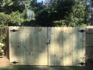 Newly installed wooden privacy fence gates with decorative black hardware, demonstrating gate services by Steven's Deck and Fence Staining Columbus, GA.