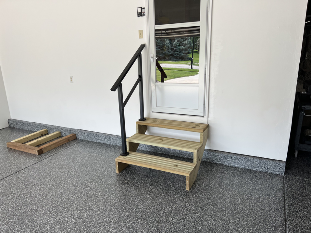 New wooden steps and a black metal handrail installed inside a garage by Folmar's Handyman & Remodeling in Lincoln, NE.