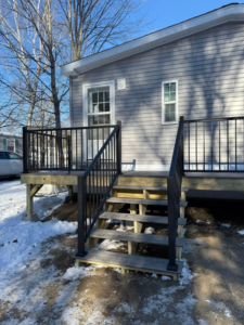 A newly built outdoor deck with black railings and stairs on a house exterior by The Finish Group in Bangor, ME.