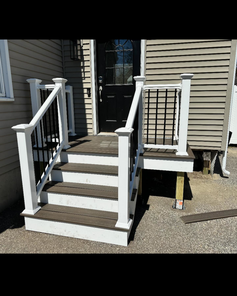 A newly built front porch with white railings and dark steps, completed by Blackcap Handyman in Portland, ME.