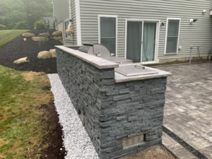 A newly built outdoor kitchen and grill island with stone veneer and paved patio by Burton Restoration LLC in Bend, OR.