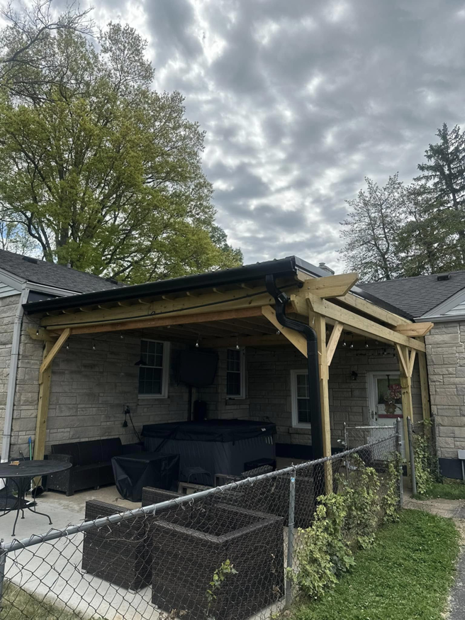 A newly built wooden pergola and patio cover with gutters attached to a stone house by J & J Remodeling of Kentucky LLC in Louisville, KY.