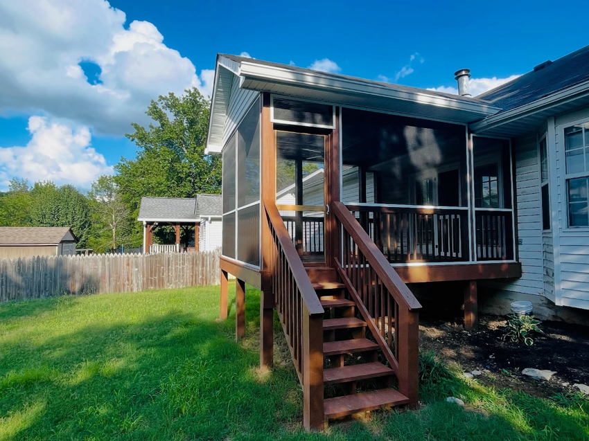 A newly built screened-in porch and deck with wooden stairs leading to a green lawn by Music City Home Experience in Nashville, TN.