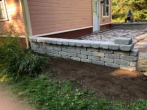 A newly built stone retaining wall providing landscaping support next to a house by Senn II Excavating in Montague, MA.