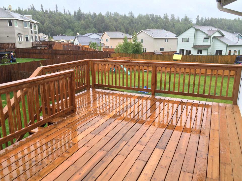 A newly built wooden deck, wet from rain, overlooking a backyard, constructed by Ground Up Services in Anchorage, AK.