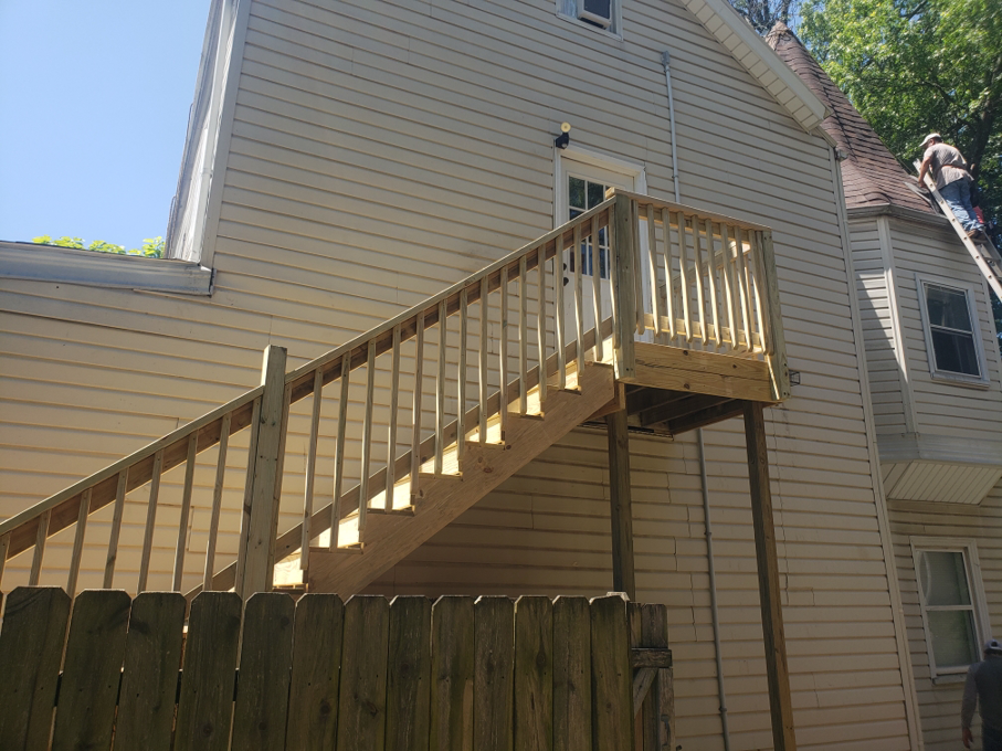 A newly built wooden deck with stairs attached to a house, with a worker on a ladder, by A1 Roofing in Scottsdale, AZ