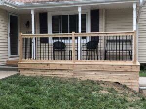 A newly built wooden porch with black metal railings in front of a house by E.L. Construction in Kansas City, MO.