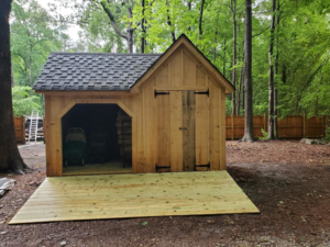 A newly built wooden shed with a shingled roof and an attached wooden deck by WHE Construction in Virginia Beach, VA