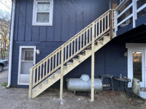A newly built wooden outdoor staircase attached to a dark blue house by Shepard Remodeling in Huntsville, AL.