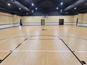 A newly finished indoor basketball court with wood-look flooring and court lines by Simply Construction in Las Vegas, NV.