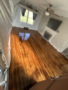 A room with newly finished, glossy hardwood floors and protective wall sheeting, completed by NV Floors LLC in Pittsburgh, PA.