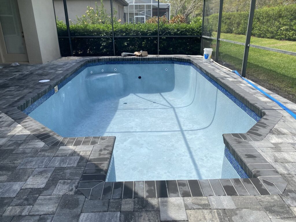 A newly finished swimming pool with fresh plaster, coping, and surrounding pavers, completed by JJB Pools & Spas in Tampa, FL.