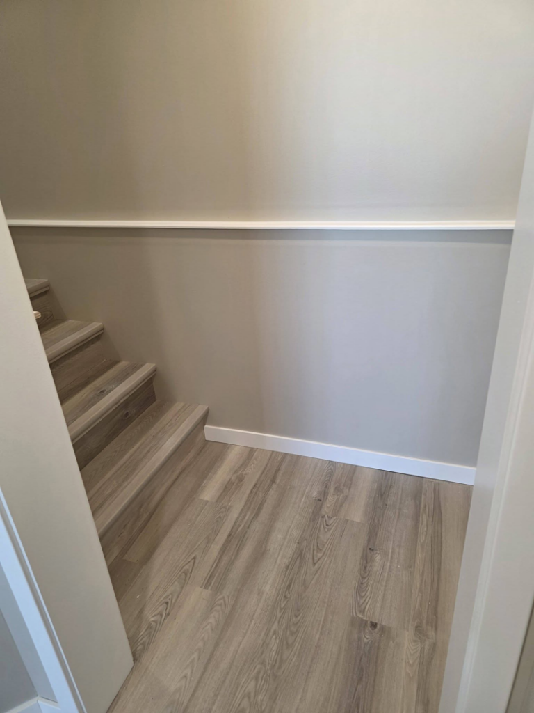 A newly finished staircase with wood-look flooring, baseboard, and chair rail by Rosenthal Remodeling in Milton, WI.
