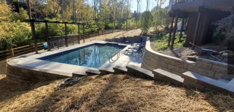 A newly installed backyard pool with surrounding landscaping and retaining walls by Heatwave Pools LLC in Flint, MI.