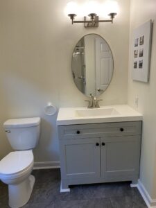 A newly installed bathroom vanity with a white sink, modern faucet, oval mirror, and toilet by Coastal Home Improvements in Greenwood, DE.