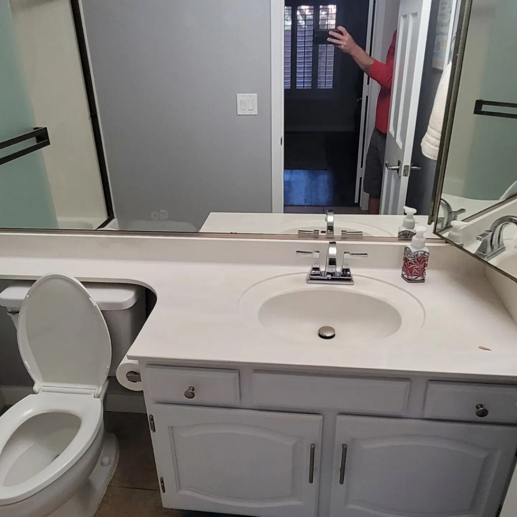 A newly installed bathroom vanity, sink, and toilet by Tier 1 Contracting Inc. in Apache Junction, AZ, reflecting a person taking the photo.
