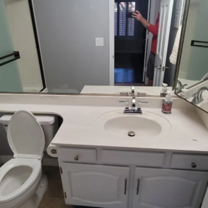 A newly installed bathroom vanity, sink, and toilet by Tier 1 Contracting Inc. in Apache Junction, AZ, reflecting a person taking the photo.