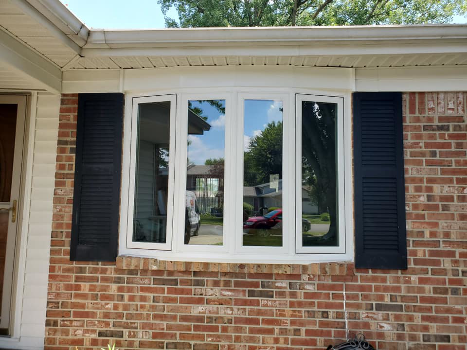 A newly installed bay window with white trim and black shutters on a brick house exterior by Hack's Construction & Window Co in Fishers, IN