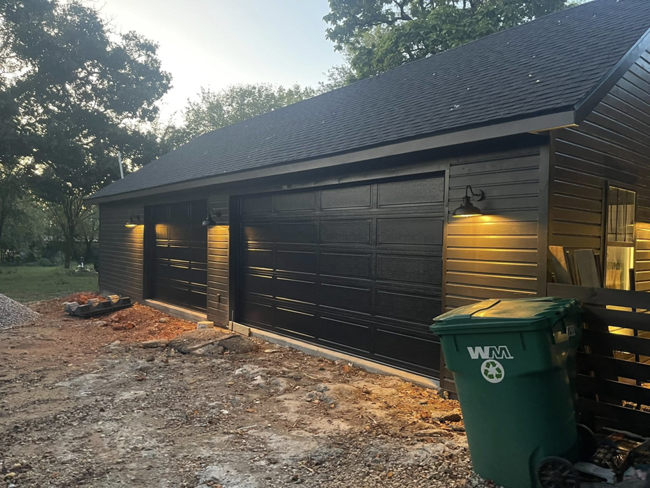 Newly installed black garage doors and exterior lighting on a building by Old Things Created New Handyman Service in Springdale, AR.