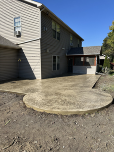 A newly installed concrete patio with a rounded edge next to a house by Lafayette Concrete & Remodel, LLC in Lafayette, IN