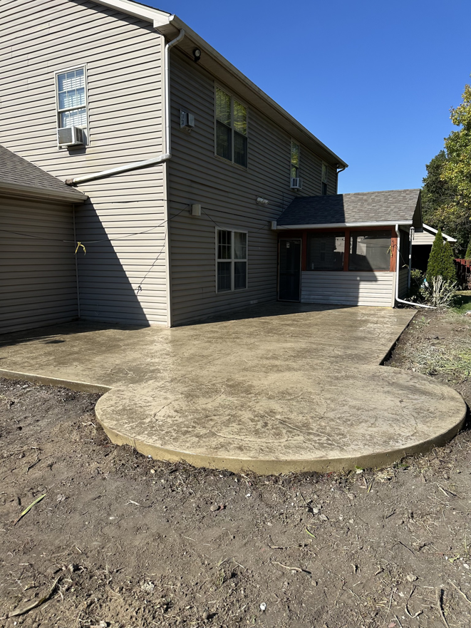 A newly installed concrete patio with a rounded edge next to a house by Lafayette Concrete & Remodel, LLC in Lafayette, IN