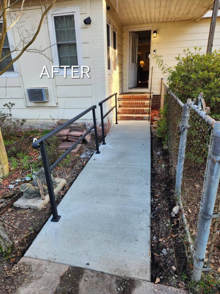 A newly installed concrete accessibility ramp with black metal handrails leading to a house entrance by Black Vault Construction Group LLC in Rock Hill, SC