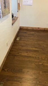 A room with a newly installed light-colored hardwood floor and an extension cord, indicating ongoing work by IHS flooring LLC in Brighton, CO.