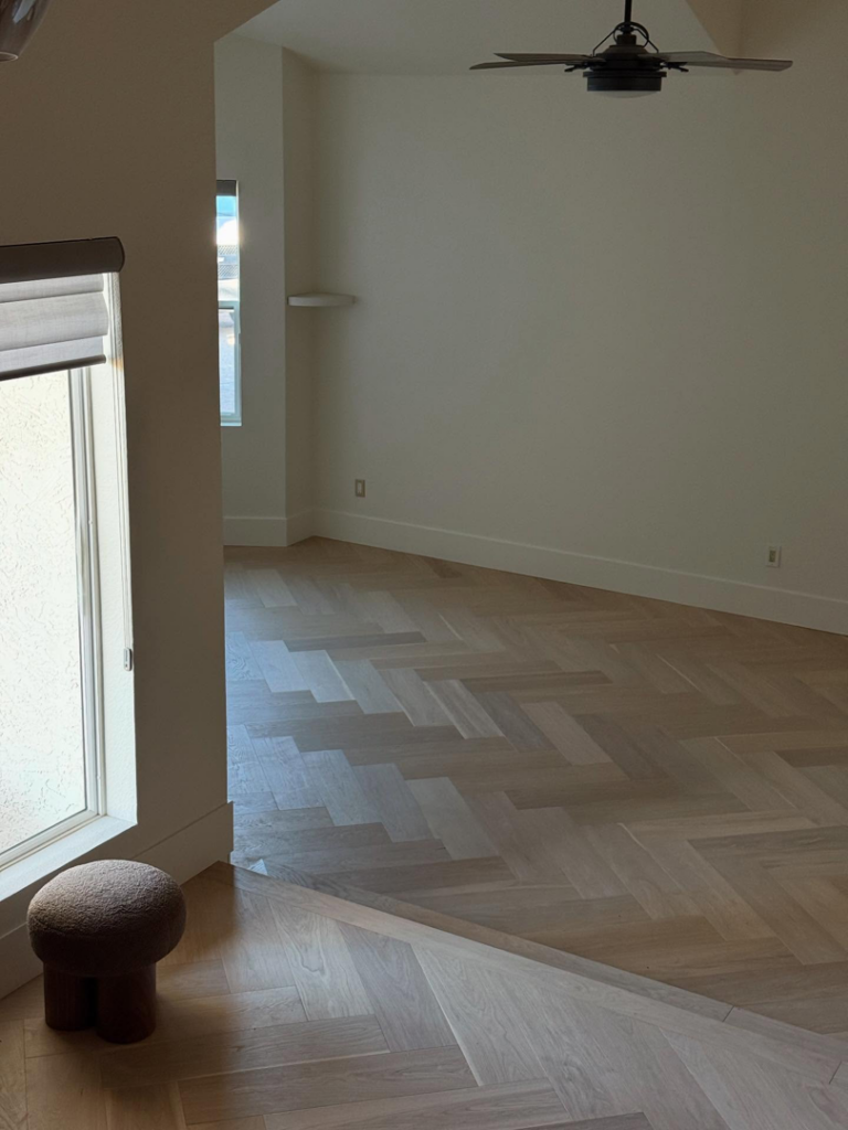 A newly installed herringbone pattern hardwood floor in a spacious room by Arizona Prestige Flooring in Surprise, AZ