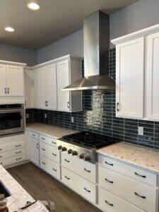 A newly installed kitchen featuring white cabinets, black subway tile backsplash, and a stainless steel range hood by Wam Bam Handyman LLC in Colorado Springs, CO