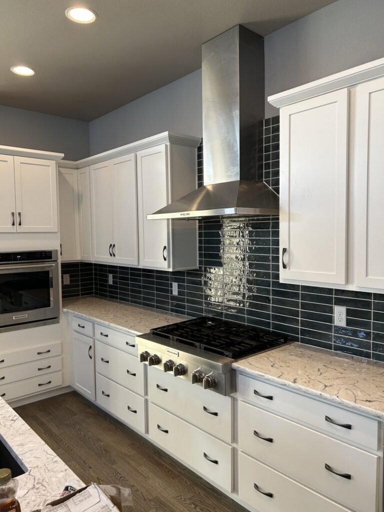 A newly installed kitchen featuring white cabinets, black subway tile backsplash, and a stainless steel range hood by Wam Bam Handyman LLC in Colorado Springs, CO