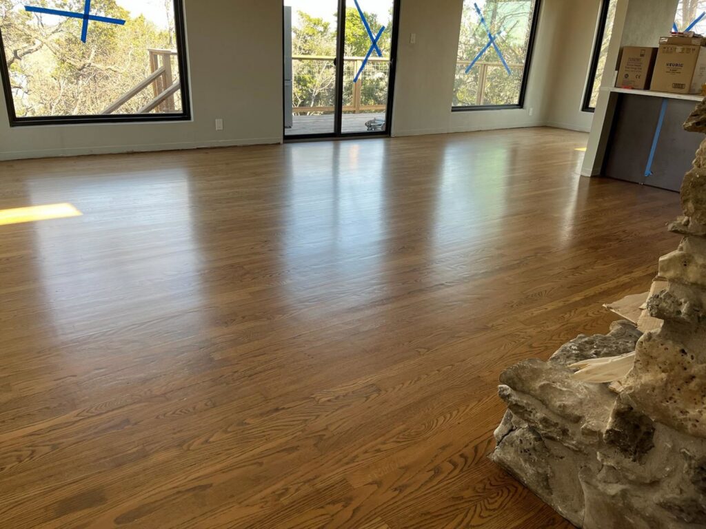 A newly installed and polished hardwood floor reflecting light in a spacious room by Burleson De Lago Real Hardwood Floors in Austin, TX.