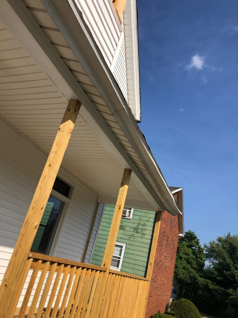 A newly installed porch roof with wooden support columns on the exterior of a house, completed by Home pro handyman llc in Olathe, KS