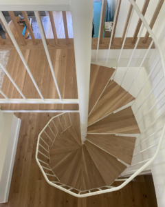 A newly installed spiral wooden staircase with white railings by Savala's Remodeling Services in Austin, TX.