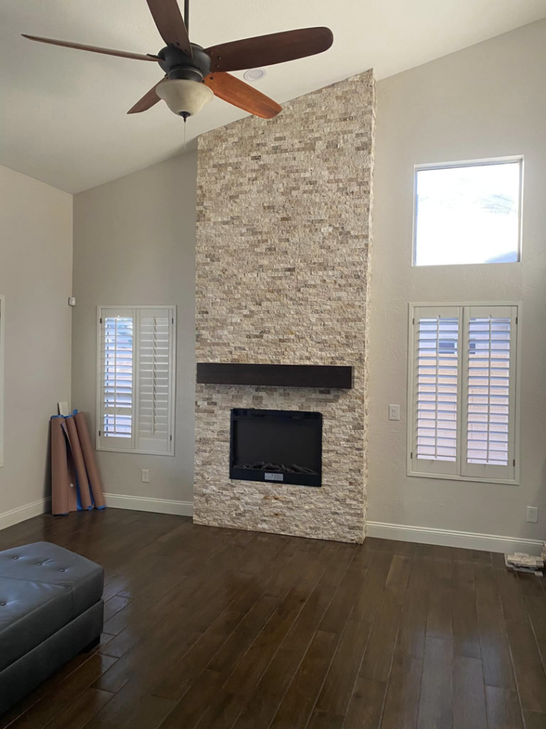 A newly installed stone fireplace and ceiling fan in a living room by Celano Construction in Mesa, AZ