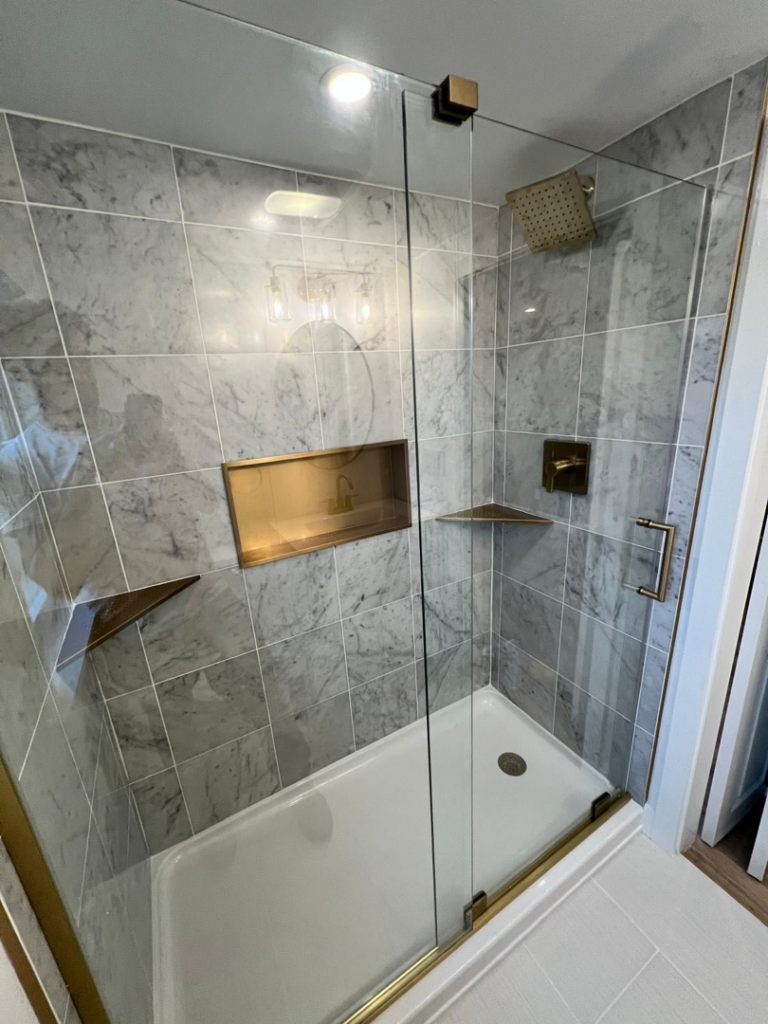 A newly installed shower with marble-look tiles, a clear glass door, and modern gold fixtures, completed by NOAT in North Providence, RI.