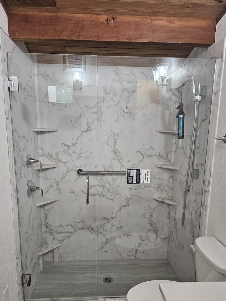 A newly installed walk-in shower with marble-patterned walls and glass doors, completed by Prestige Statewide, LLC in Eugene, OR.