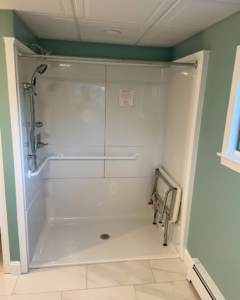 A newly installed white walk-in shower with grab bars and a folding seat, completed by Yellow Ladder Contracting in Mount Pleasant, SC