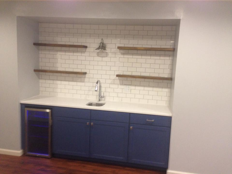 A newly installed wet bar with subway tile backsplash, blue cabinets, and floating shelves by J Development in Pittsburgh, PA.