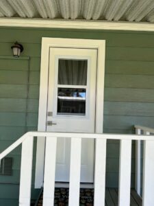 A newly installed white exterior door with a matching railing on a green house by Sal Handyman Services in Canyon Country, CA