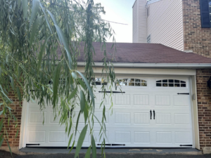 A newly installed white garage door with decorative hardware on a residential home by Advanced Garage Doors LLC in Alexandria, VA.