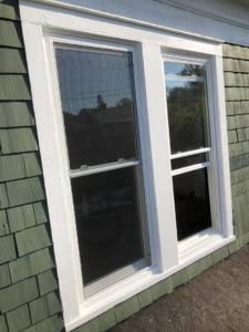 A newly installed window with white trim on a green shingle house by Harrington Home Repair LLC in Albany, NY.